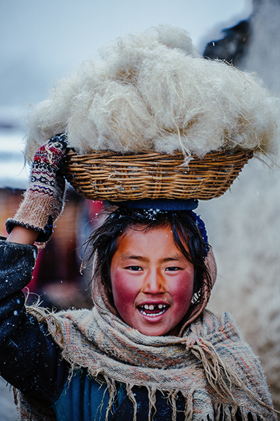 After child in a Himalayan village balances a woven basket filled with white yak wool on her head