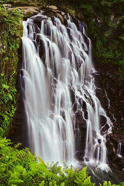 After towering waterfall plunges over multiple layers of dark, weathered rocks