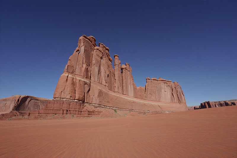 Before massive red sandstone formations rising from an orange-red desert floor