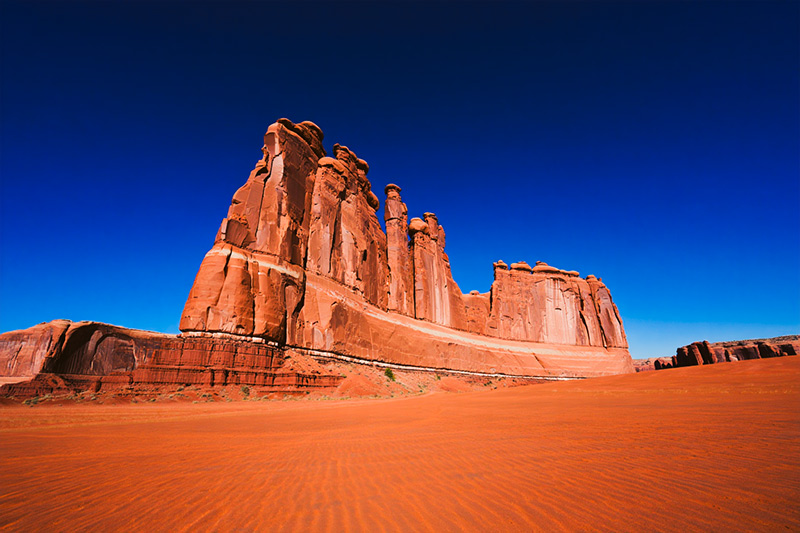 After massive red sandstone formations rising from an orange-red desert floor