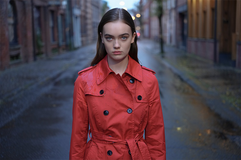 Before woman in a bright red trench coat stands confidently in the center of a wet city street