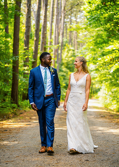 After wedding couple walking side by side down a dirt path through a sunlit forest