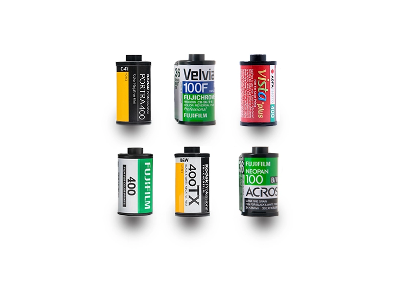 Six film canisters including Kodak Portra, Fuji Velvia and Agfa Vista laid flat on wooden surface